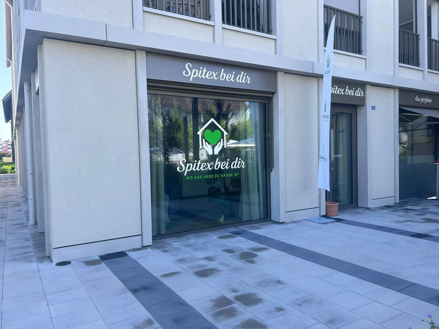 Aussenansicht des Spitex Bei dir GmbH Büros an der Dorfstrasse 13g in 8155 Niederhasli – Spitex-Stützpunkt im Zürcher Unterland mit grünem Herz-Logo im Schaufenster